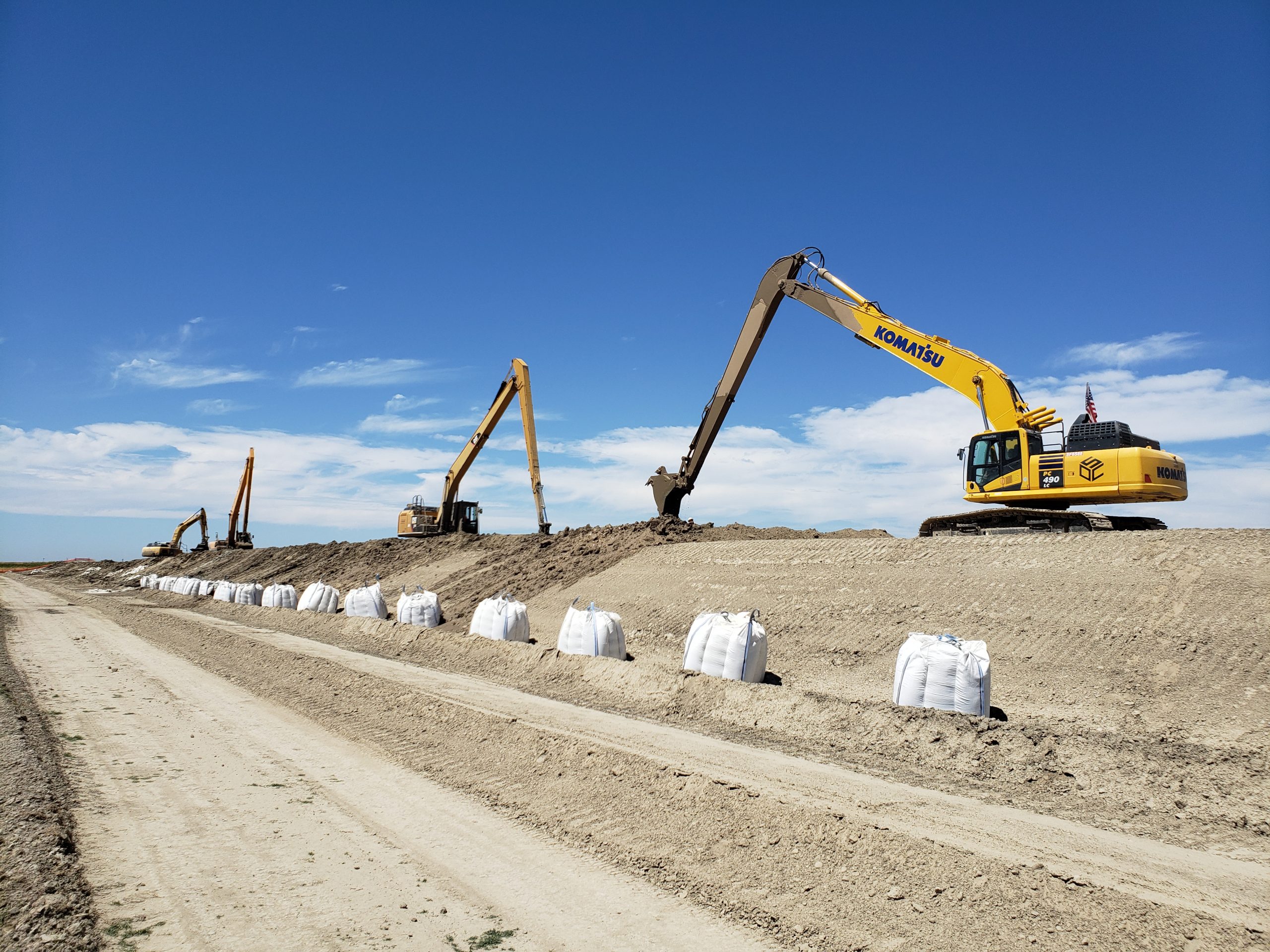A line of excavators sits atop a levee doing improvements in Reach O of the Eastside Bypass